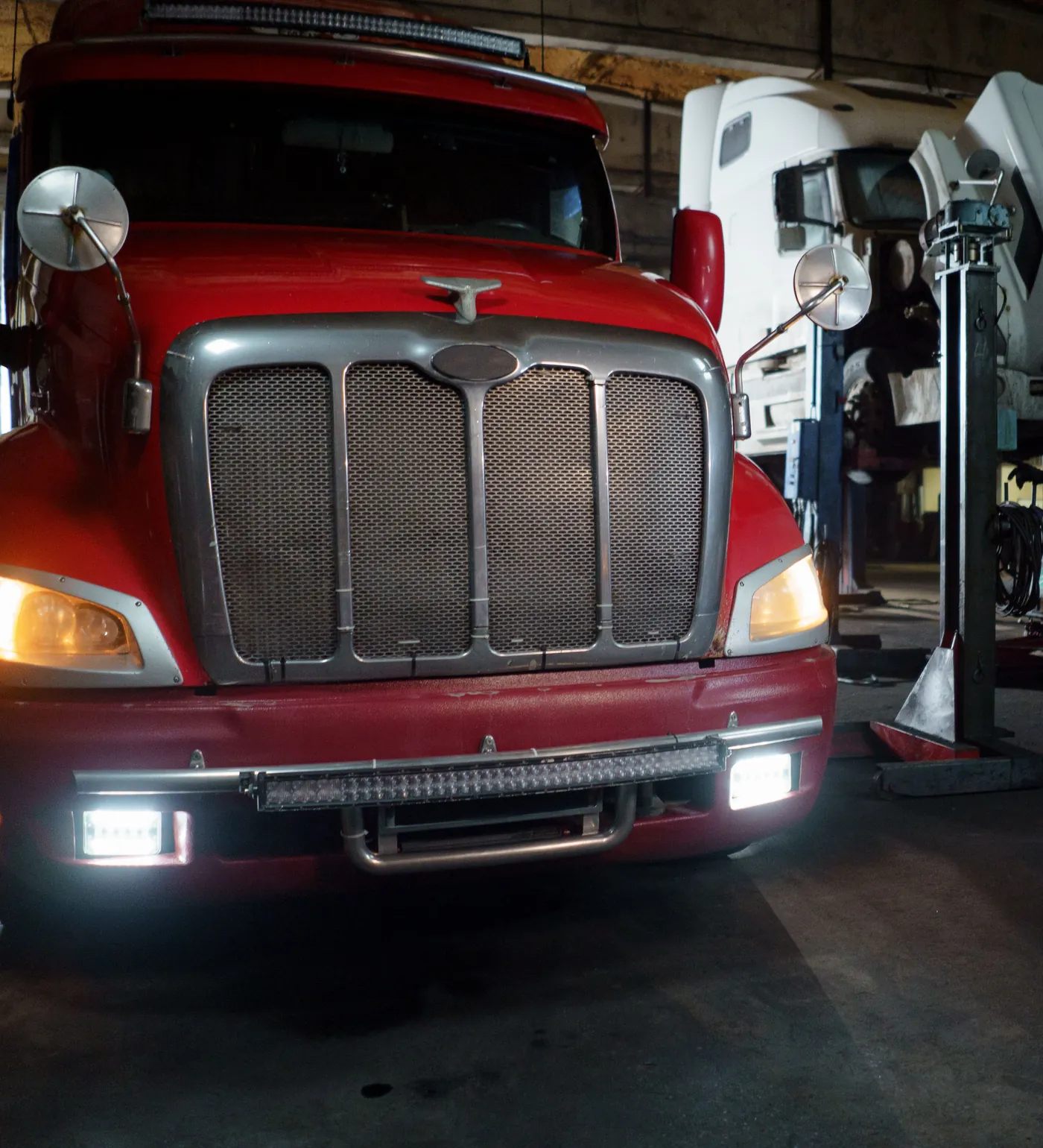A red tractor in a shop bay with a technician and lifted trucks