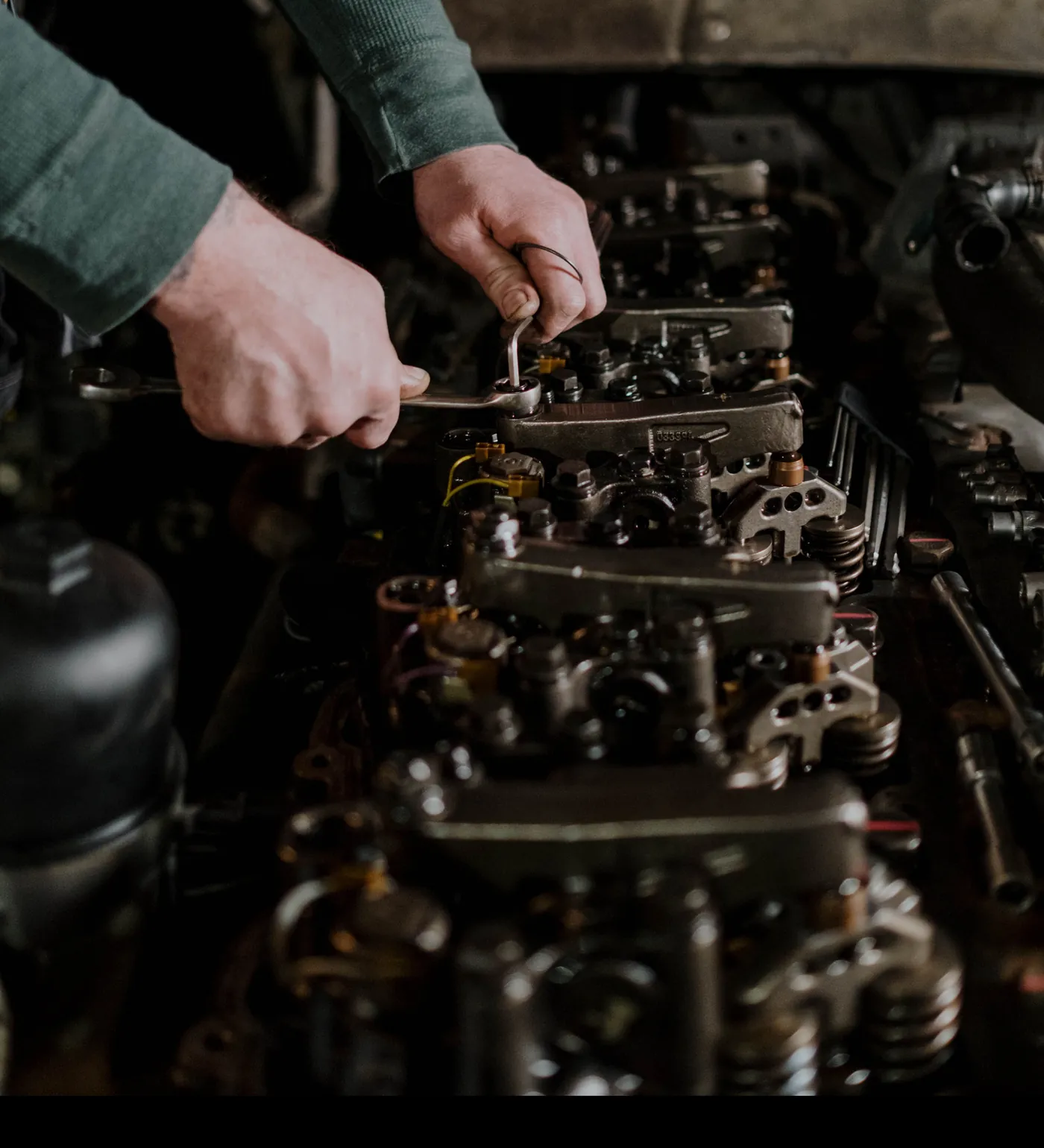 A technician with wrenches at the valve train of a diesel engine