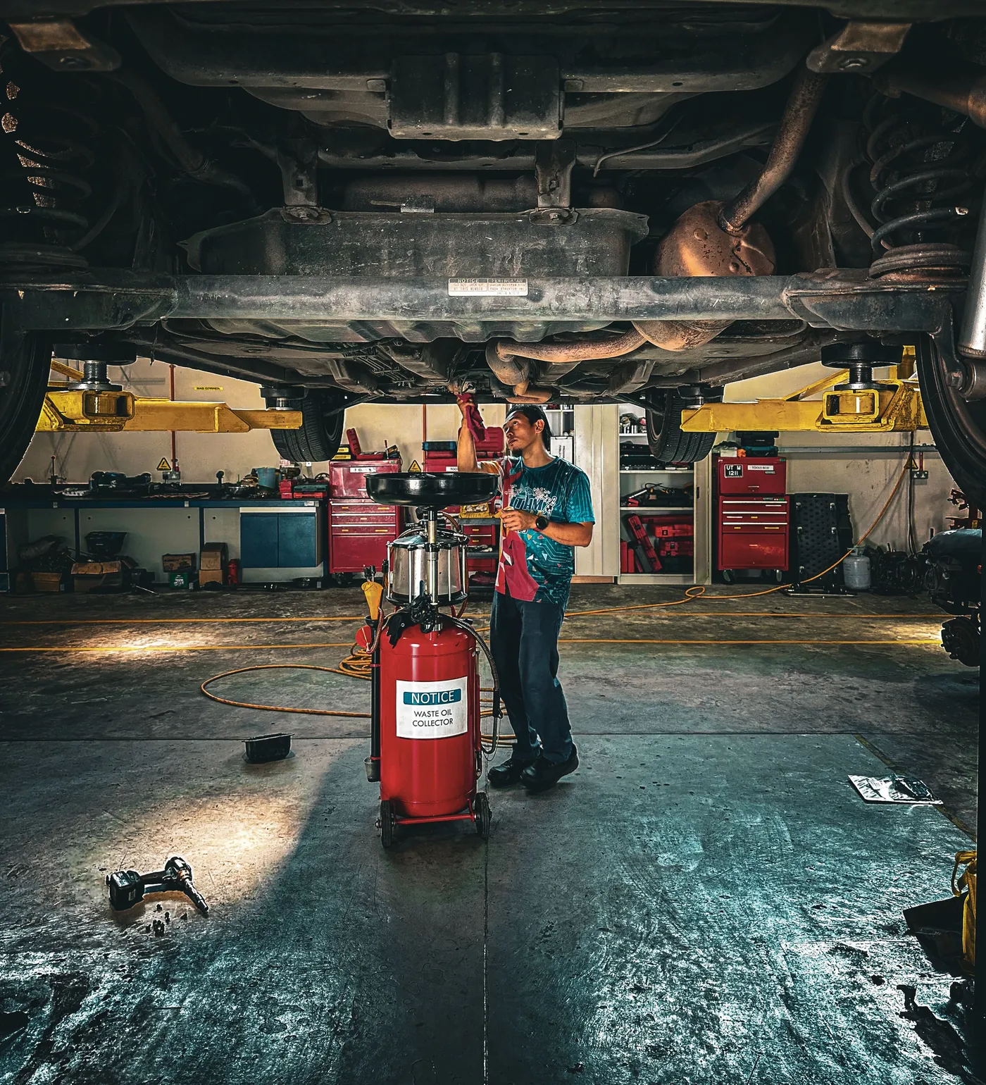 A technician under a lifted vehicle beside a waste oil collector